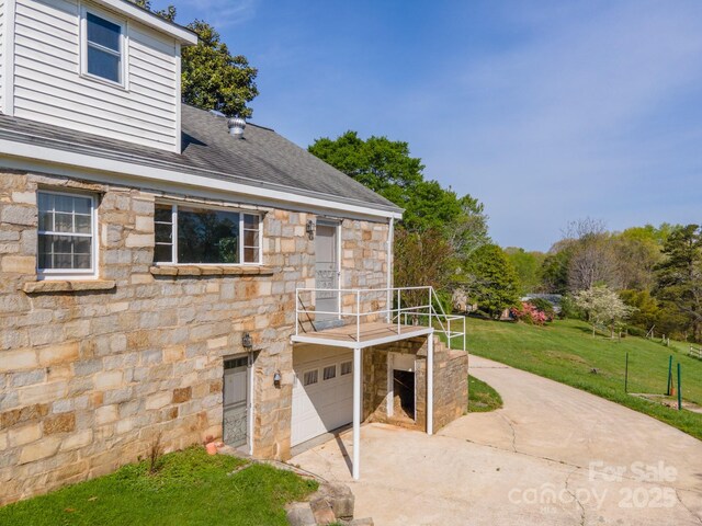 exterior space with a lawn, driveway, stone siding, an attached garage, and a shingled roof