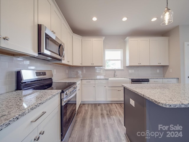 kitchen featuring appliances with stainless steel finishes, sink, tasteful backsplash, light wood-type flooring, and decorative light fixtures