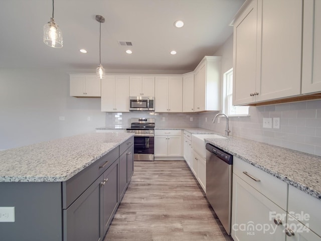 kitchen featuring decorative light fixtures, light hardwood / wood-style flooring, white cabinetry, backsplash, and stainless steel appliances