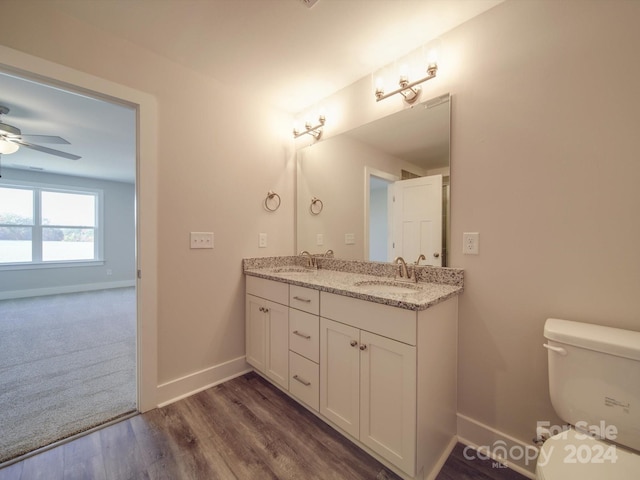 bathroom featuring wood-type flooring, ceiling fan, toilet, and dual bowl vanity