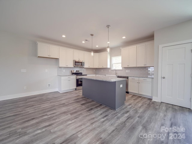 kitchen featuring appliances with stainless steel finishes, a kitchen island, white cabinets, light wood-type flooring, and decorative light fixtures