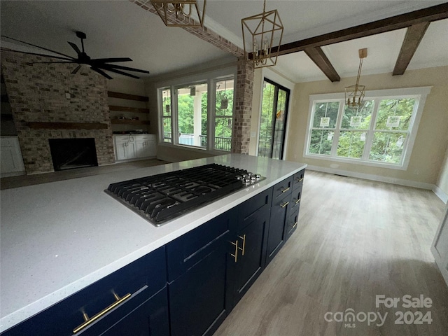 kitchen featuring decorative light fixtures, black gas stovetop, a fireplace, beamed ceiling, and light wood-type flooring