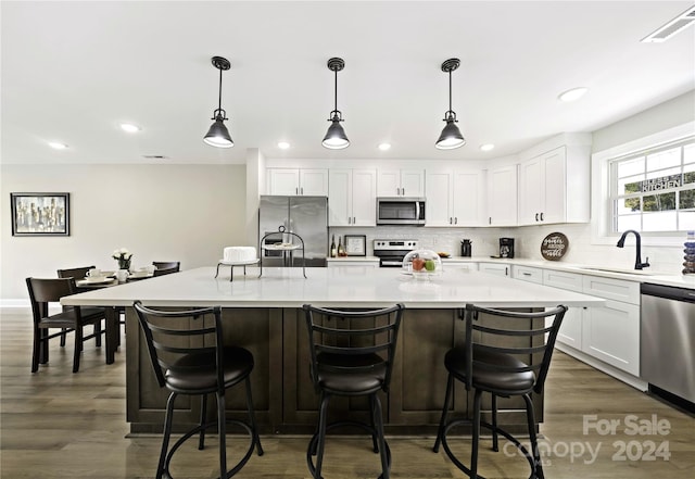 kitchen featuring stainless steel appliances, hanging light fixtures, white cabinets, and a center island