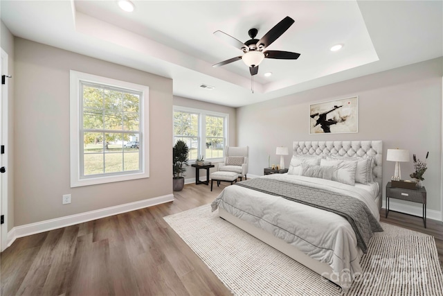 bedroom with hardwood / wood-style floors, ceiling fan, and a raised ceiling