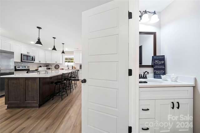 kitchen with light hardwood / wood-style floors, white cabinets, a breakfast bar area, a kitchen island with sink, and appliances with stainless steel finishes