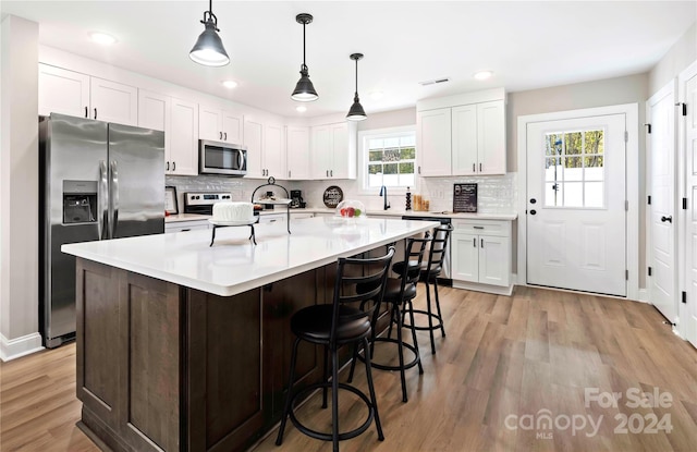 kitchen with white cabinets, stainless steel appliances, a healthy amount of sunlight, and an island with sink