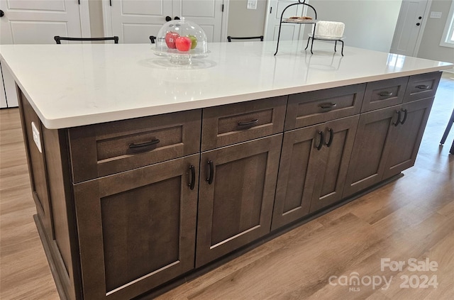 kitchen with light hardwood / wood-style flooring, dark brown cabinetry, a kitchen breakfast bar, and a spacious island