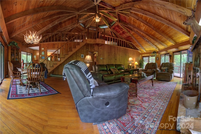 living room featuring a notable chandelier, beam ceiling, wooden walls, light hardwood / wood-style flooring, and wooden ceiling