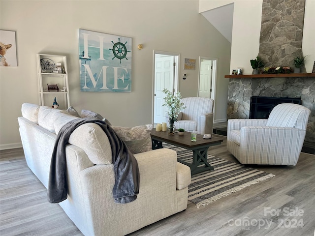 living room featuring hardwood / wood-style flooring, a stone fireplace, and high vaulted ceiling