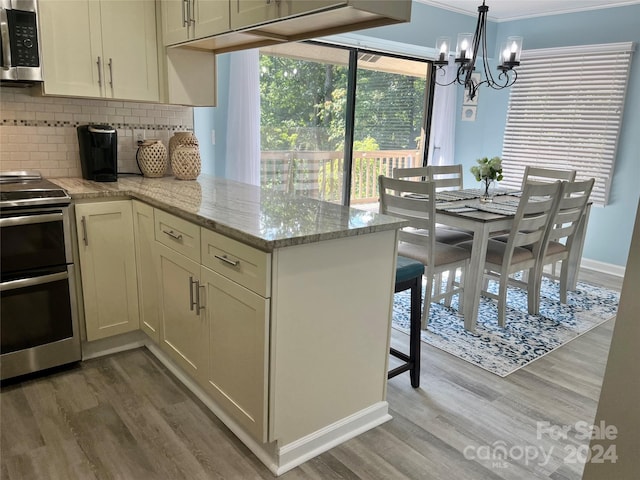 kitchen with a notable chandelier, light hardwood / wood-style floors, tasteful backsplash, stainless steel appliances, and light stone countertops