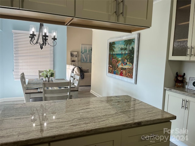 kitchen with hardwood / wood-style flooring, pendant lighting, a notable chandelier, and light stone countertops