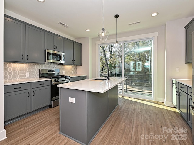 kitchen with a center island with sink, visible vents, gray cabinets, stainless steel appliances, and a sink