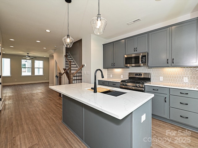 kitchen with decorative light fixtures, stainless steel appliances, visible vents, gray cabinetry, and an island with sink