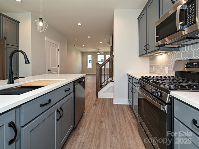 kitchen with a sink, stainless steel appliances, gray cabinetry, pendant lighting, and backsplash