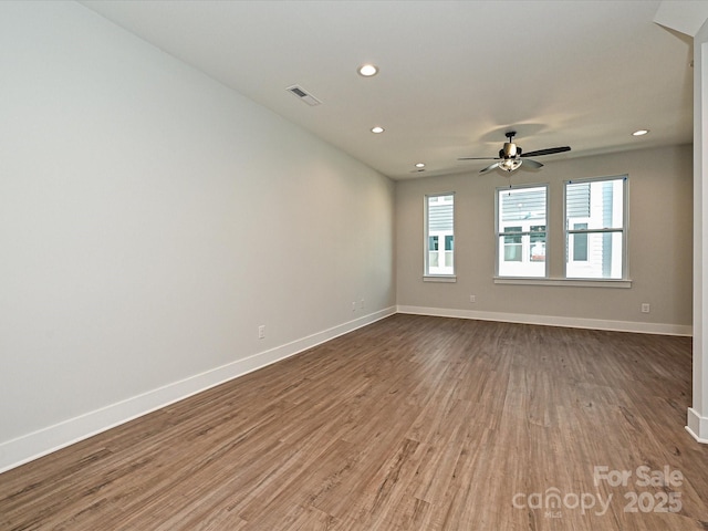 empty room with wood finished floors, visible vents, and baseboards