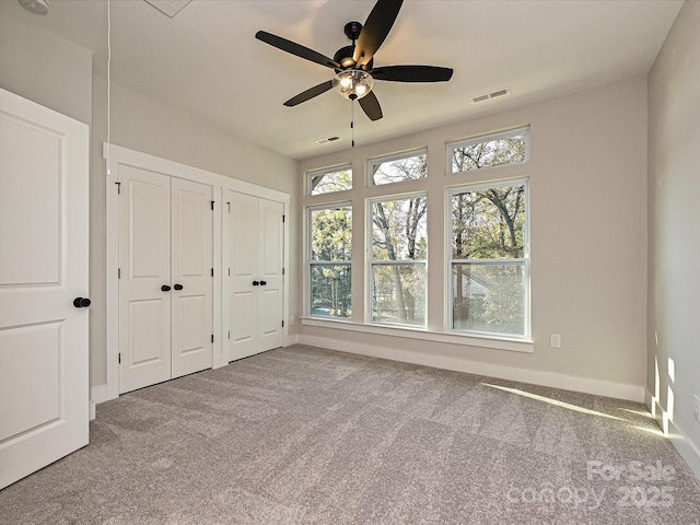 unfurnished bedroom featuring light carpet, baseboards, visible vents, and two closets