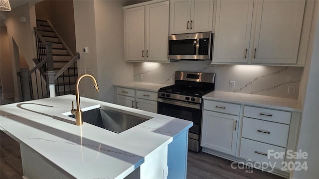 kitchen featuring sink, dark hardwood / wood-style floors, a center island with sink, white cabinets, and appliances with stainless steel finishes