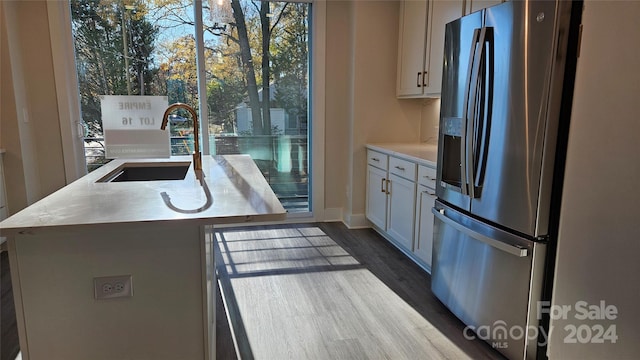 kitchen with white cabinetry, sink, dark hardwood / wood-style floors, stainless steel refrigerator with ice dispenser, and a center island with sink