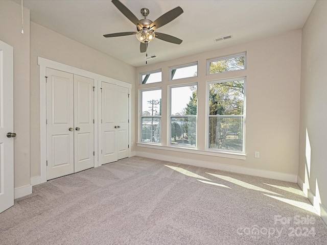 unfurnished bedroom with light colored carpet, ceiling fan, and multiple closets