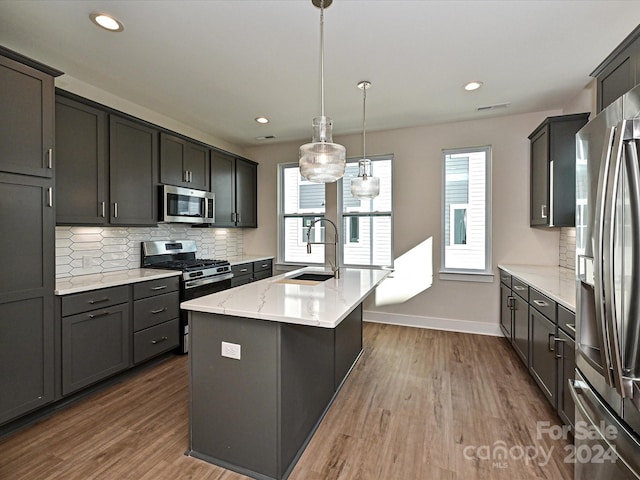 kitchen with appliances with stainless steel finishes, a kitchen island with sink, dark wood-type flooring, sink, and decorative light fixtures