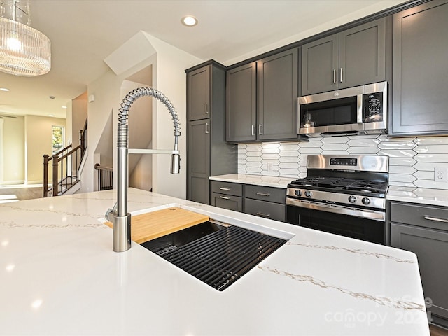 kitchen featuring light stone countertops, appliances with stainless steel finishes, tasteful backsplash, sink, and decorative light fixtures