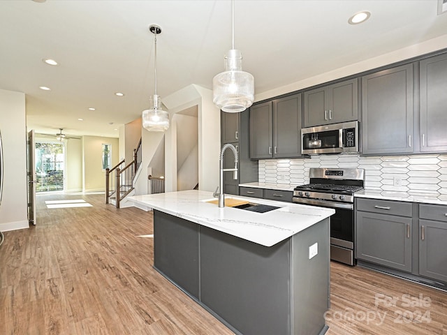 kitchen featuring sink, hanging light fixtures, light wood-type flooring, an island with sink, and stainless steel appliances