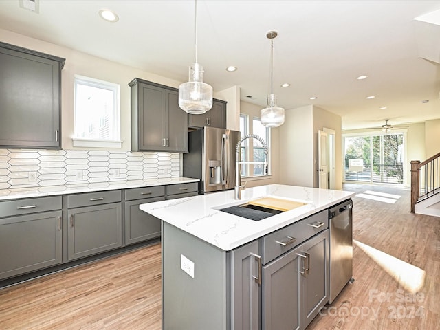 kitchen featuring gray cabinetry, a center island with sink, hanging light fixtures, sink, and appliances with stainless steel finishes