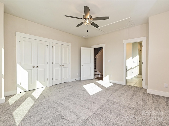 unfurnished bedroom featuring ceiling fan, light colored carpet, connected bathroom, and multiple closets