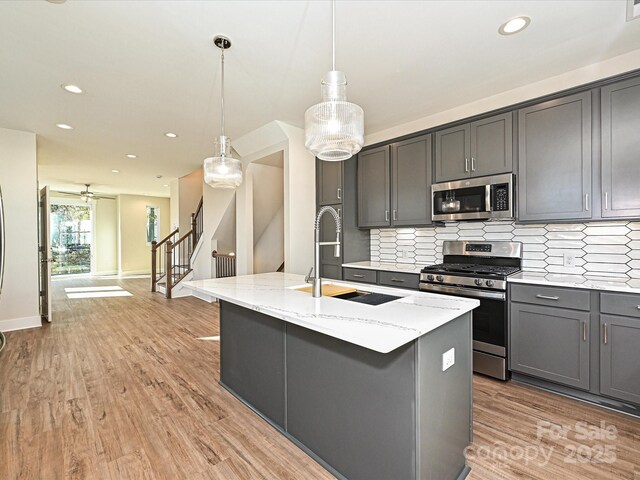 kitchen with light stone counters, stainless steel appliances, a sink, decorative backsplash, and gray cabinetry