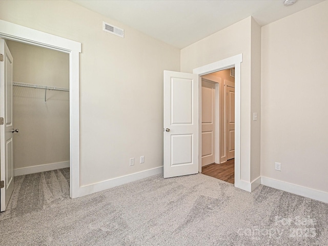 unfurnished bedroom with a spacious closet, baseboards, carpet flooring, and visible vents