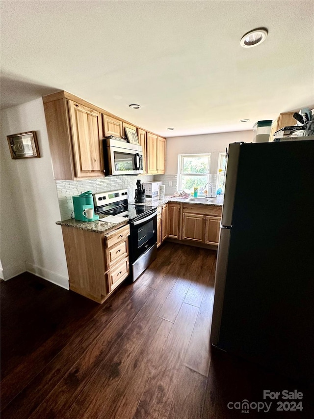 kitchen featuring tasteful backsplash, dark hardwood / wood-style floors, dark stone countertops, sink, and appliances with stainless steel finishes