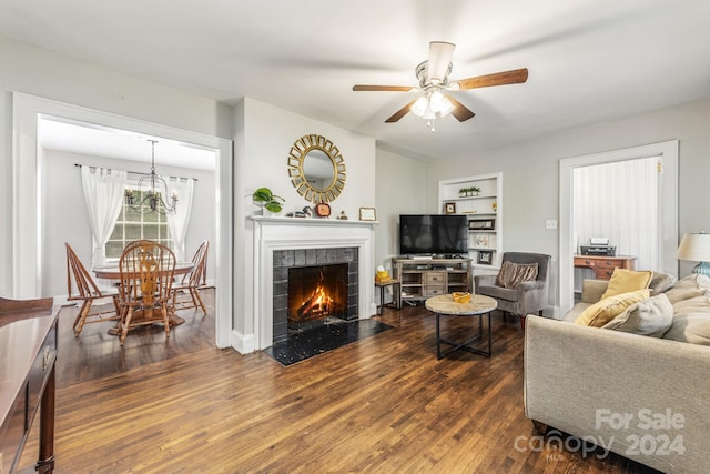 living room with ceiling fan, a tiled fireplace, dark hardwood / wood-style flooring, and built in shelves