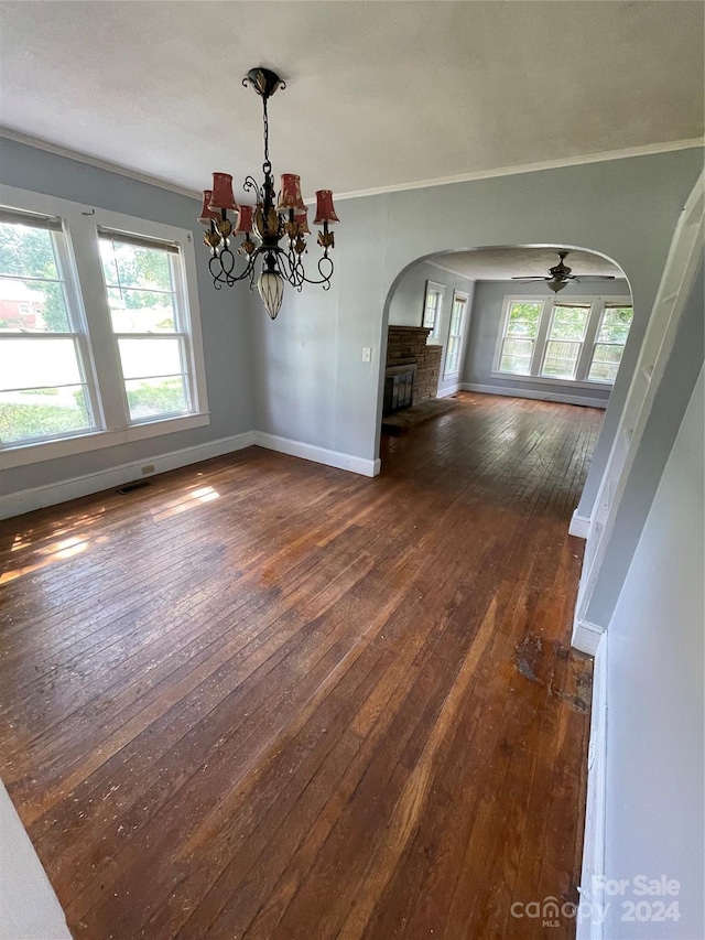 unfurnished dining area with a fireplace, dark hardwood / wood-style flooring, ceiling fan with notable chandelier, and crown molding