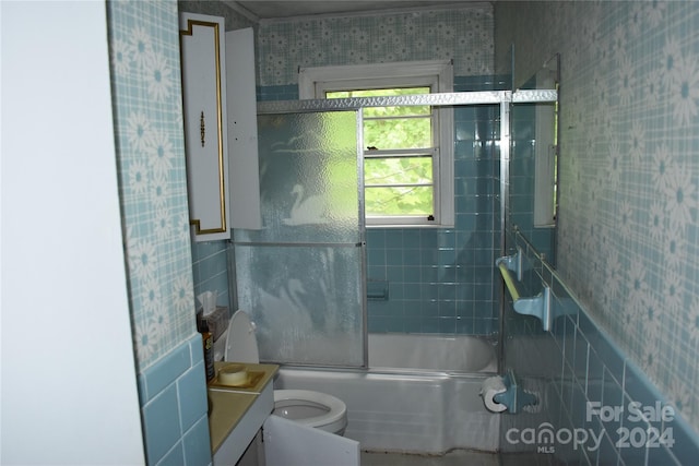 full bathroom featuring tile walls, bath / shower combo with glass door, toilet, and vanity