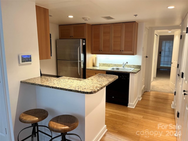 kitchen with a breakfast bar area, black dishwasher, stainless steel fridge, and light wood-type flooring