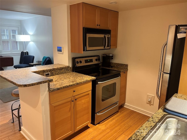 kitchen with kitchen peninsula, light wood-type flooring, light stone counters, a breakfast bar area, and appliances with stainless steel finishes