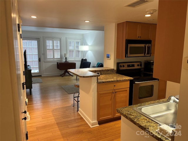 kitchen featuring a kitchen breakfast bar, stainless steel appliances, light hardwood / wood-style floors, and kitchen peninsula