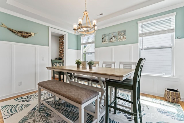 dining space with a notable chandelier, a raised ceiling, brick wall, and light wood-type flooring