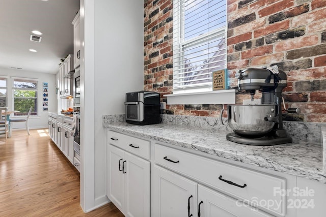 kitchen with white cabinetry, light hardwood / wood-style floors, brick wall, light stone counters, and stainless steel oven