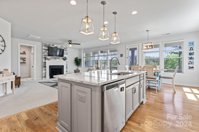 kitchen with hanging light fixtures, light wood-type flooring, stainless steel dishwasher, a kitchen island with sink, and sink