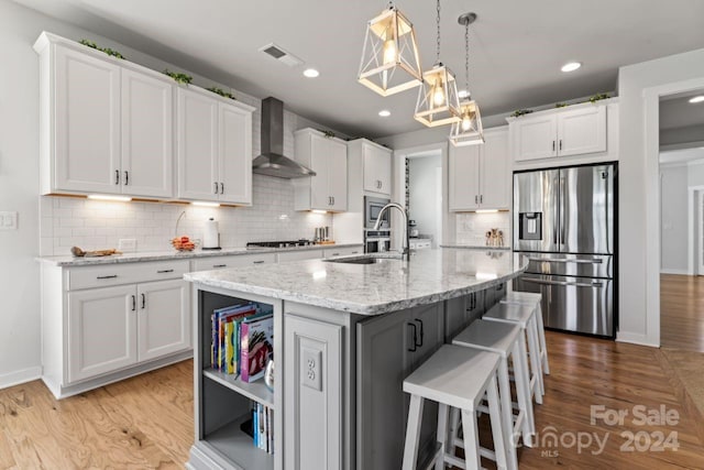 kitchen featuring wall chimney range hood, stainless steel appliances, light wood-type flooring, and backsplash