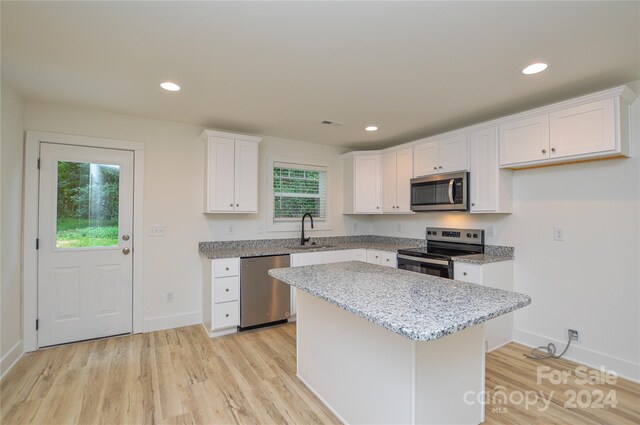 kitchen with appliances with stainless steel finishes, light hardwood / wood-style floors, white cabinetry, sink, and light stone countertops