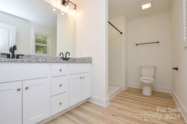 bathroom with hardwood / wood-style floors, double sink vanity, toilet, and walk in shower