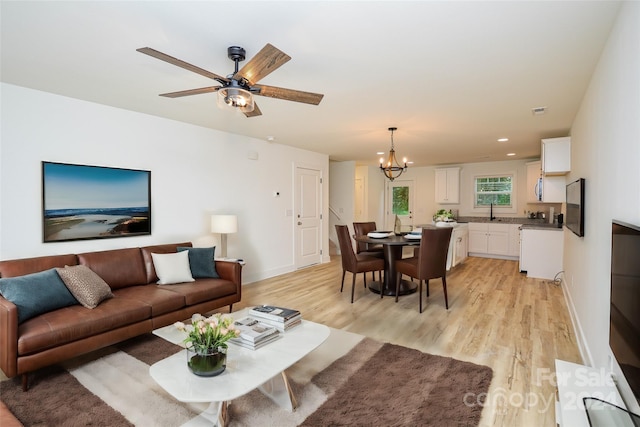 living room featuring baseboards, light wood finished floors, and ceiling fan with notable chandelier