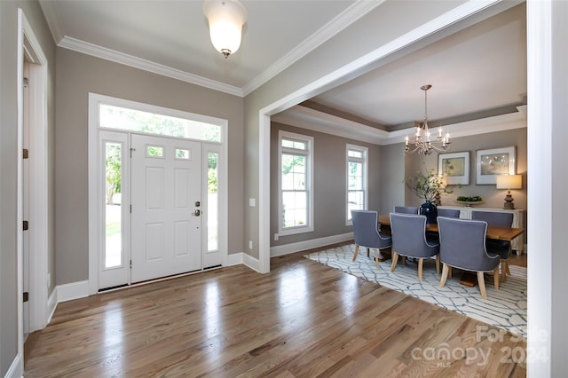 foyer entrance featuring hardwood / wood-style floors, a tray ceiling, crown molding, and a chandelier