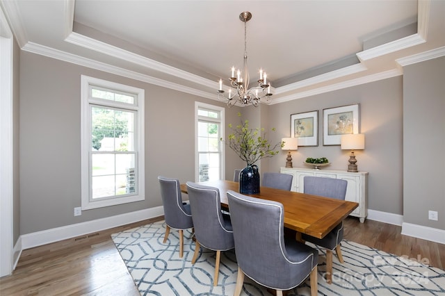 dining space featuring wood-type flooring, a raised ceiling, ornamental molding, and an inviting chandelier