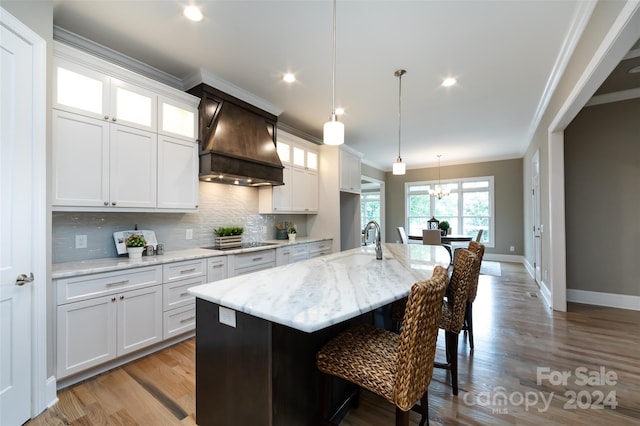 kitchen with premium range hood, tasteful backsplash, a kitchen island with sink, white cabinets, and sink