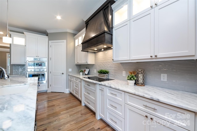 kitchen with stainless steel double oven, pendant lighting, white cabinets, sink, and custom range hood