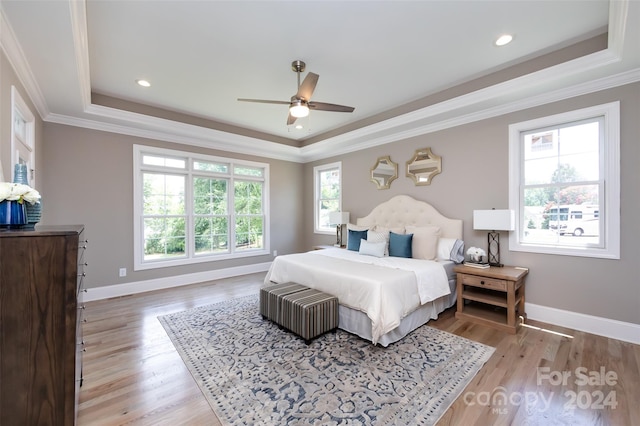 bedroom featuring light wood-type flooring, ceiling fan, a tray ceiling, and multiple windows