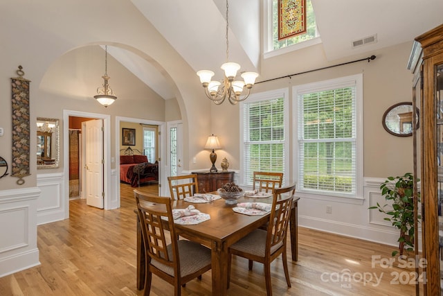 dining area with high vaulted ceiling, an inviting chandelier, and light wood-type flooring